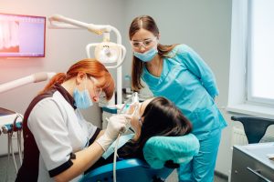 Female dentist and a nurse in masks and protective glasses performing patient's dental checkups